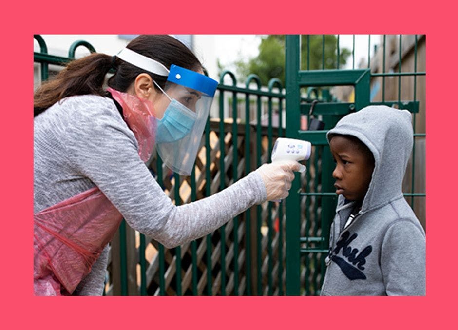 A woman wearing personal protective equipment including a mask, takes a child's temperature in a school playground. 
