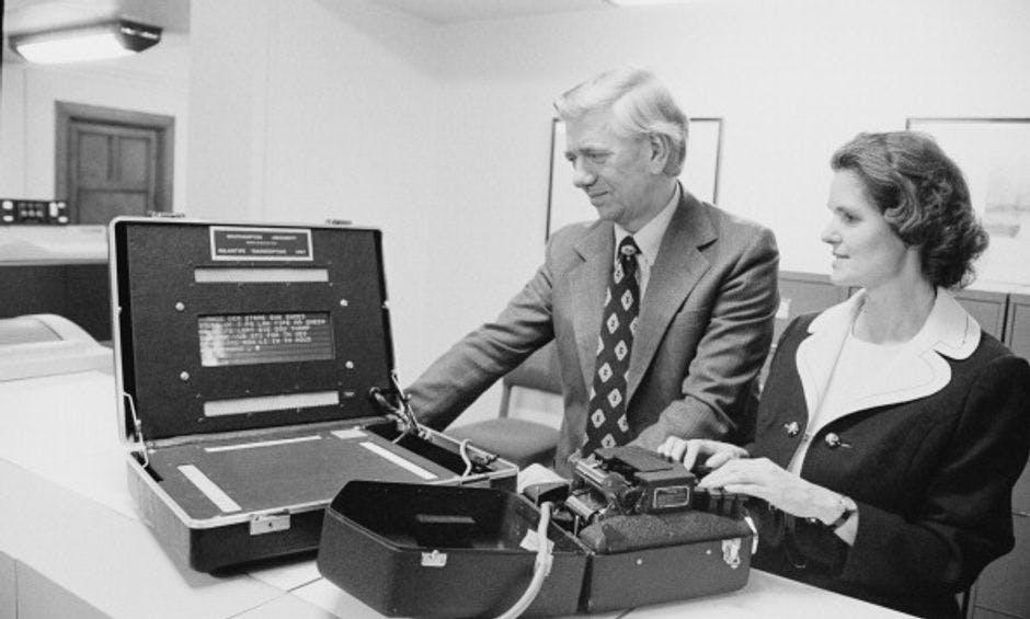 A man and a woman standing next to a briefcase containing an electronic device